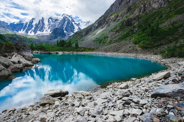 El lago de montaña está rodeado de grandes piedras y cantos rodados frente al hermoso glaciar gigante. Increíbles montañas nevadas. Cresta de nieve. Maravilloso paisaje atmosférico de majestuosa naturaleza de las tierras altas.