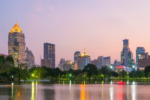 Lago en el parque de Lumpini con el edificio alto del distrito del centro de negocios de Bangkok en fondo en la puesta del sol.