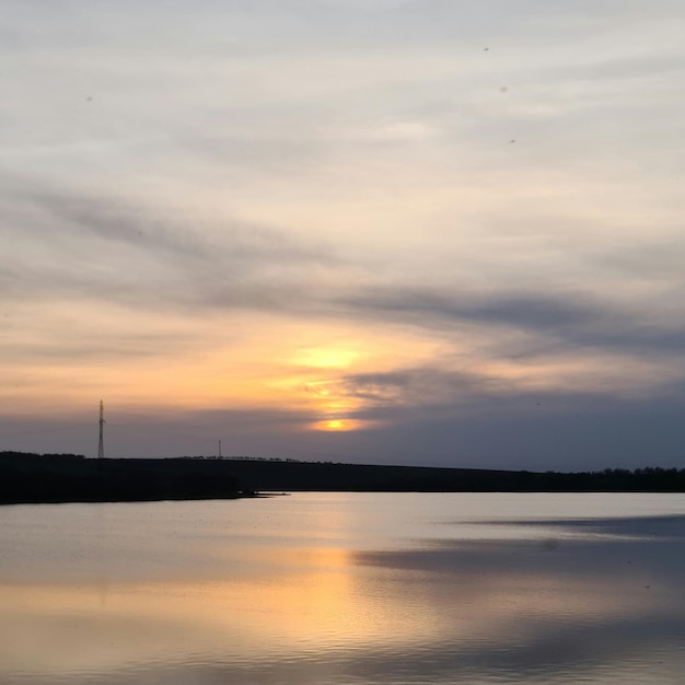 Un lago con una puesta de sol y una torre al fondo