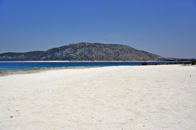 Lago Salda con arena blanca, agua azul y montañas al fondo en un día soleado, Turquía