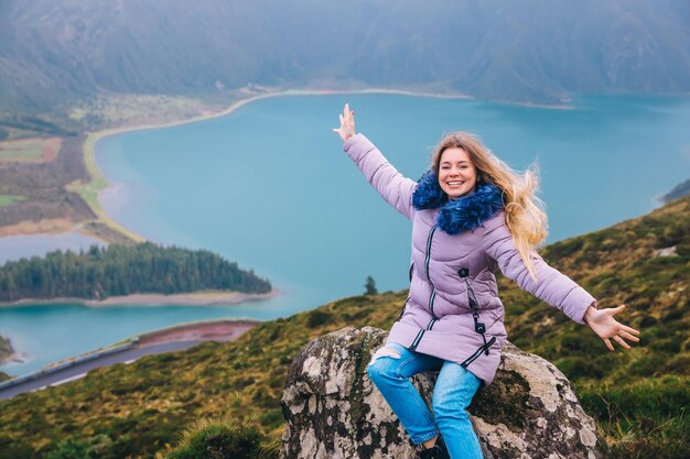 Lagoa do Fogo nublado durante las vacaciones de primavera en el área de Acores San Miguel La niña se divierte con los brazos extendidos sentada sobre una piedra en las montañas