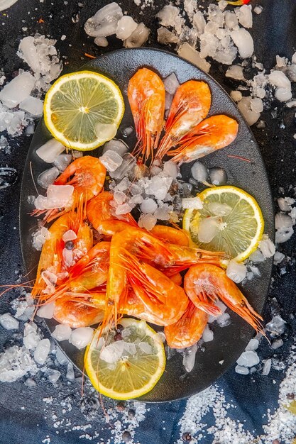 Foto lagostins de camarão vermelho descascados, limão, sal marinho grande, deitado em uma tábua escura com verduras