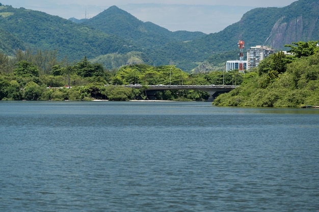 Laguna de Marapendi con edificios, vegetación y árboles alrededor. Colinas y puente Barra da Tijuca al fondo. Ubicado cerca de Praia da Reserva en Río de Janeiro.