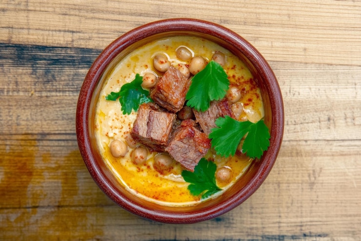 Foto laham bil hummus servido en un plato hondo de barro con carne y garbanzos frescos