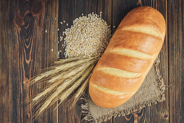 Laib Brot und Ähren auf dunklem Holzhintergrund.