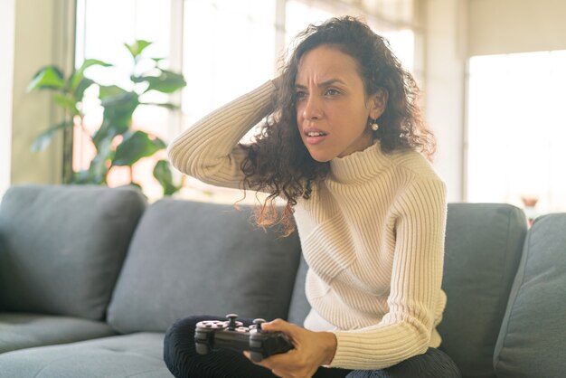 Laitin-Frau, die Videospiele mit den Händen spielt, die Joystick auf dem Sofa zu Hause halten