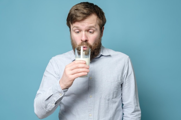 Laktoseintoleranz Ein verwirrter bärtiger Mann blickt nachdenklich auf ein Glas Milch in seiner Hand