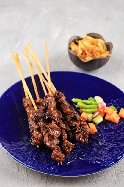 Lamm-Satay oder Sate-Kambing-Fleisch-Satay, serviert mit gewürfeltem Acar-Lamm, gegrillt mit süßer Sojasauce auf blauem Teller, selektiver Fokus