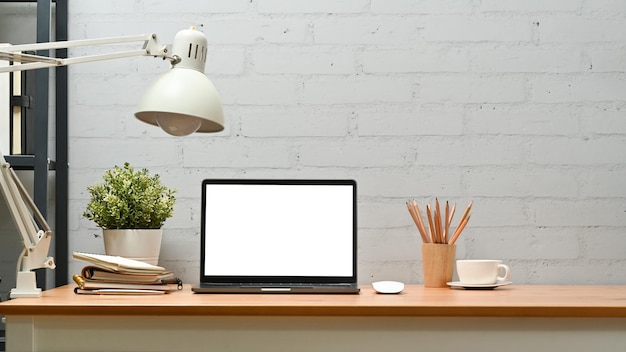 Lâmpada de vaso de computador portátil e suprimentos na mesa de madeira contra a parede de tijolos Tela em branco para anunciar o design