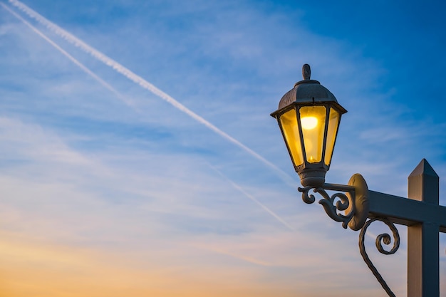 Lâmpada elétrica em estilo retrô em um poste de madeira A lâmpada brilha contra o fundo do céu com nuvens durante o pôr do sol Ideia para fundo de férias ou espaço de cópia de cartão postal para texto