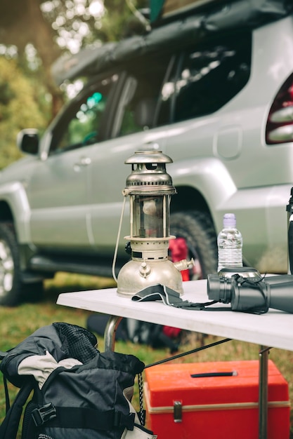 Foto lámpara de aceite y binoculares sobre mesa de camping en el bosque con vehículo todoterreno en el fondo