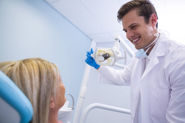 Lámpara de ajuste del dentista mientras mira al paciente en la clínica médica