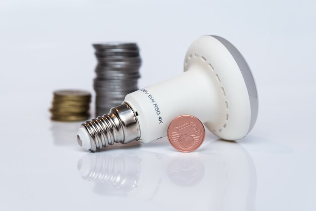 La lámpara económica LED se apoya en una superficie blanca junto a las monedas