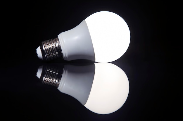 La lámpara LED está encendida sobre un fondo oscuro con reflejos en la superficie. ahorro en electricidad. industria electrica