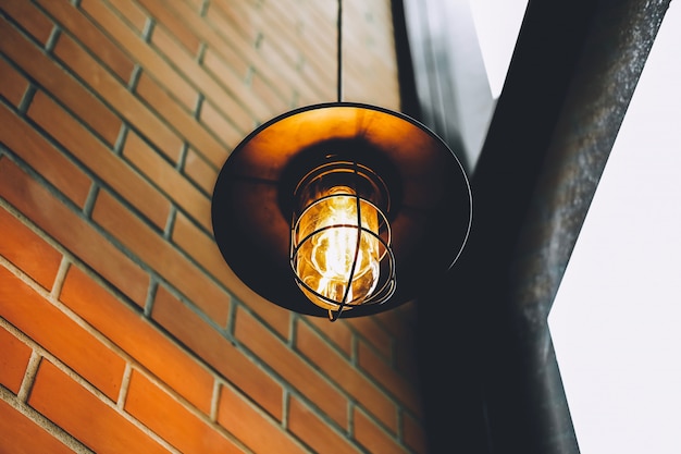Lámpara LED vintage o bombilla incandescente en restaurante o cafetería con pared de bloque antiguo con tono marrón y naranja.