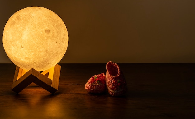 Lámpara de luna y zapatilla de bebé en mesa de madera