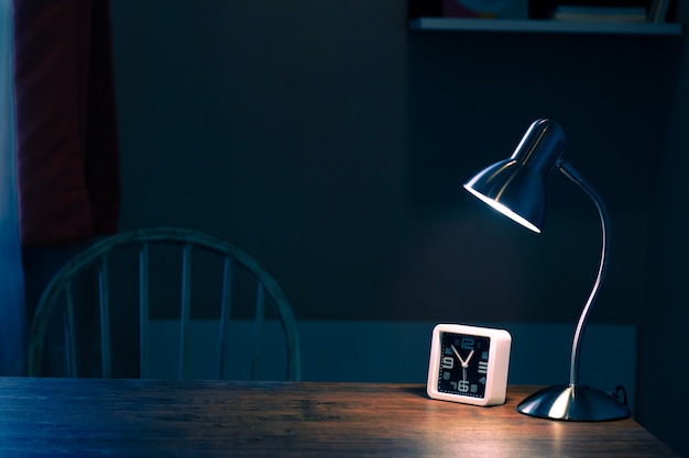 Foto lámpara de mesa pequeña y reloj de escritorio en mesa de madera por la noche