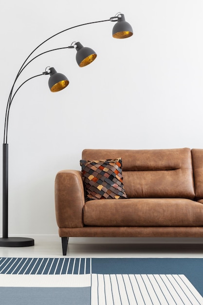 Lámpara moderna junto al sofá de cuero en el interior de la sala de estar blanca con alfombra estampada Foto real