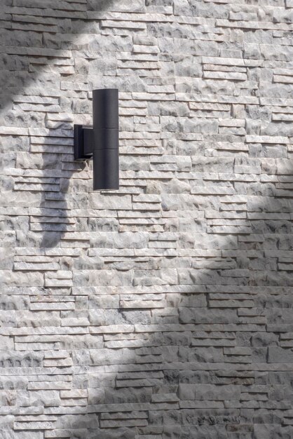 Lámpara de pared cilíndrica negra para exteriores sobre fondo de pared de ledgestone blanco y gris vintage