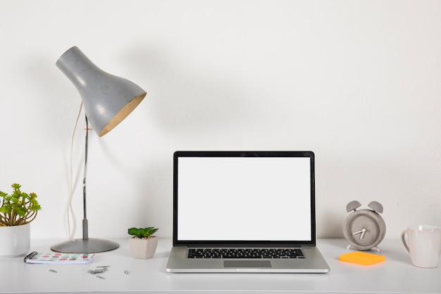 Lámpara y plantas cerca de la computadora portátil y el despertador