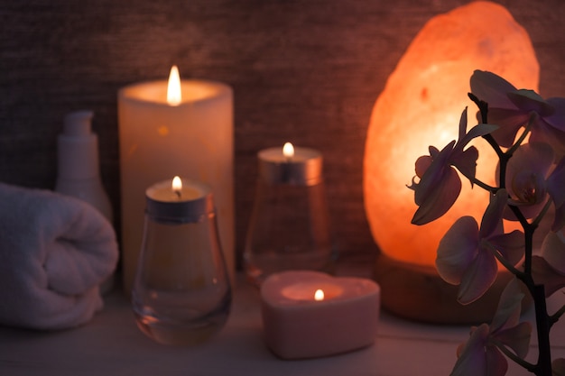 Lámpara de sal del Himalaya con flor de orquídea, aceite, toalla, velas en una habitación oscura.