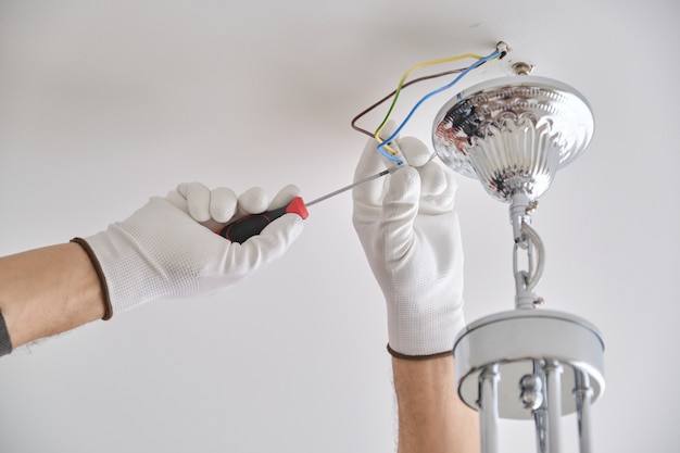 Lámpara de techo de instalación, manos de electricista masculino que fija la lámpara con el uso de herramientas profesionales