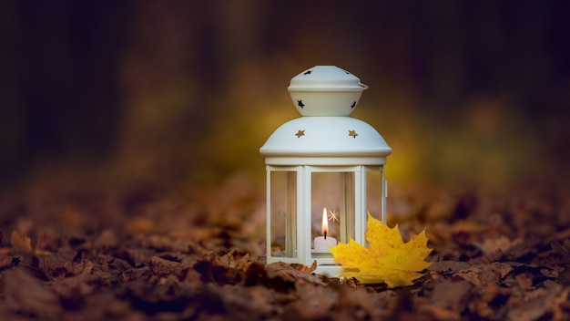 Lámpara con una vela por la noche sobre una hoja seca de otoño.