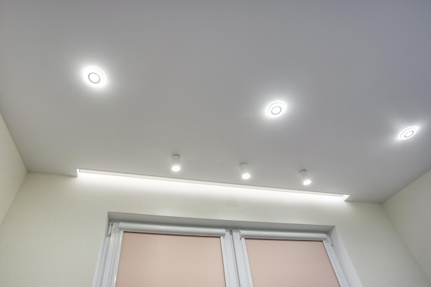 Lámparas halógenas en techo suspendido y construcción de paneles de yeso en una habitación vacía en un apartamento o casa Techo tensado blanco y forma compleja