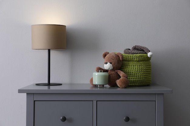 Lampe child39s Spielzeug und Weidenkorb auf Kommode in der Nähe von hellgrauer Wand im Innenbereich