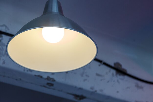 Lampe im Schatten an alter strukturierter Decke. Beleuchtungsvorrichtung auf schäbigem Hintergrund