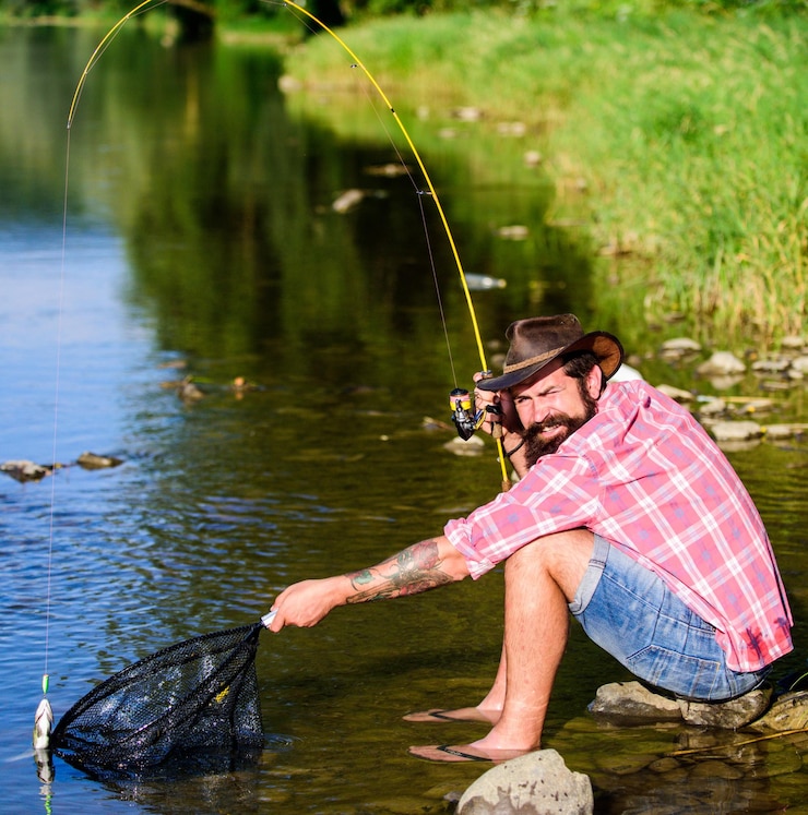 Foto lançando aquele peixe fora do homem com peixe na vara pesca esportiva relaxar na natureza pescador bem sucedido na água do lago hipster pescando com isca de colher peixe com mosca passatempo do homem hipster em camisa quadriculada