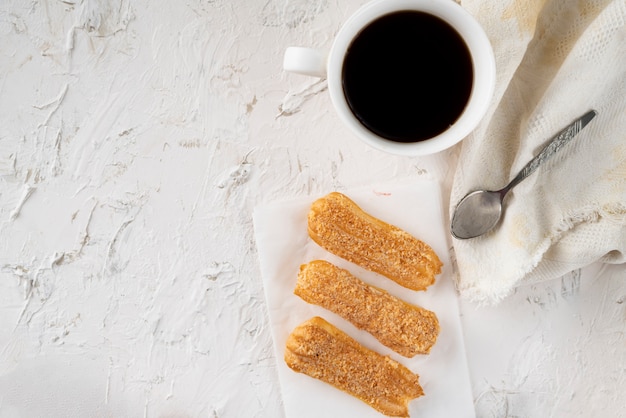 Lanche da manhã com café e eclair cremoso em uma mesa com toalha de mesa branca, café da manhã de negócios