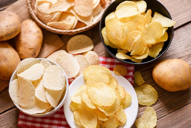 Lanche de batatas fritas na tigela e prato Batatas fritas crocantes na mesa da cozinha e batatas cruas frescas em fundo de madeira