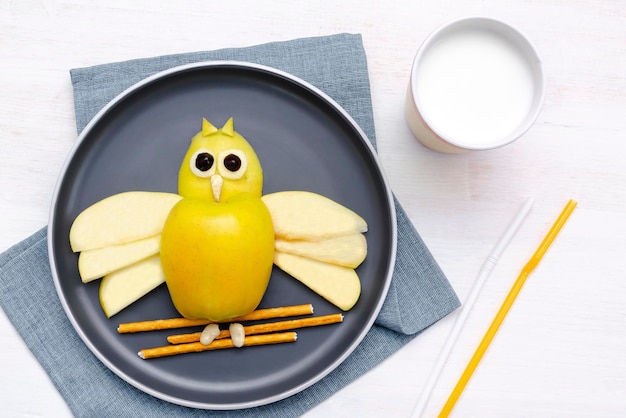 Lanche em forma de rosto de coruja engraçado com palha de pão crocante de trigo de maçã na chapa leite em vidro Sobremesa doce de bebê infantil bonito arte de comida de almoço saudável em fundo de madeiravista superior