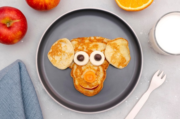 Lanche engraçado em forma de rosto de macaco de panqueca no prato Crianças fofas sobremesa doce de bebê para crianças café da manhã saudável arte de comida com milkapplesorange no fundo de concreto cinzavista superior