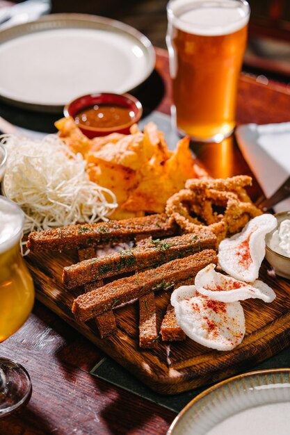 Lanche para cerveja em uma tábua de madeira Croutons de batata e arroz chips anéis de cebola queijo defumado molho de tomate e molho tártaro Servido no pub