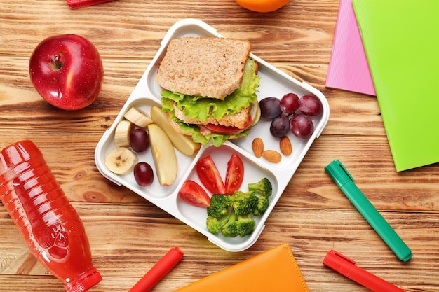 Foto lancheira com comida deliciosa e artigos de papelaria em fundo de madeira