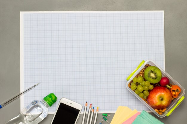 Lancheira com frutas e nozes, papel em branco, smartphone e garrafa de água