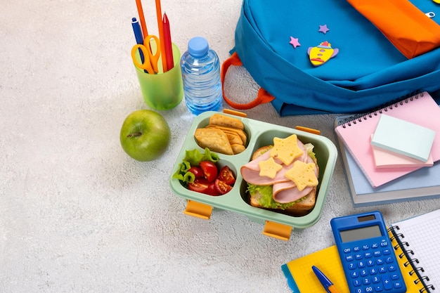 Lancheira escolar saudável com sanduíche e salada no local de trabalho perto de mochila Material escolar livros maçã e uma garrafa de água