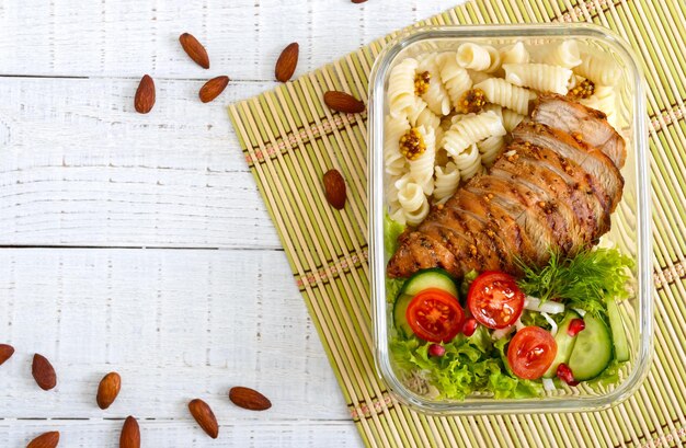 Lancheira: rotini com peito de frango assado e salada em um fundo branco de madeira. Vista superior, postura plana. Delicioso almoço saudável. O conceito de alimentação saudável.