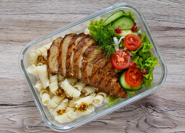 Lancheira: rotini com peito de frango assado e salada em um fundo de madeira. Vista superior, postura plana. Delicioso almoço saudável. O conceito de alimentação saudável.