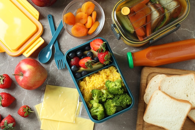 Lancheiras com comida saborosa em mesa texturizada cinza