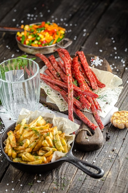 lanches de carne para cerveja, ao lado de um copo de cerveja, batatas fritas em uma panela, em uma mesa rústica de madeira