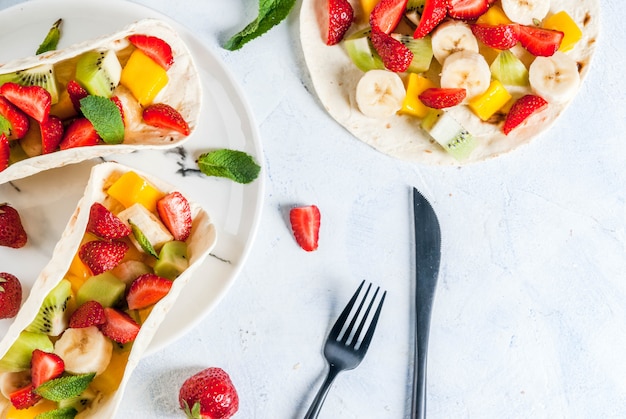 Lanches de verão. Comida para uma festa. Tacos de frutas com morangos, mangas, bananas, chocolate, menta. Em uma mesa de concreto azul claro. vista superior copyspace