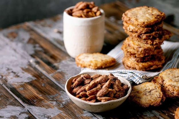 Lanches doces caseiros. Tigela de mel glaceado, amêndoas torradas, nozes e biscoitos de açúcar amanteigados quadrados na mesa de madeira escura. Doces clássicos. Copie o espaço