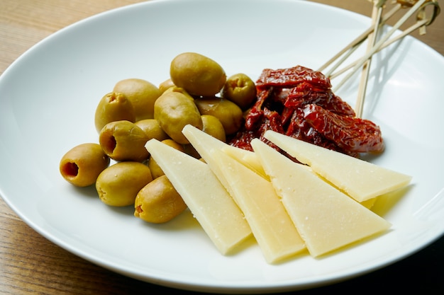 Lanches para o jantar. prato de antepastos com azeitonas, queijo duro e tomate seco. visão