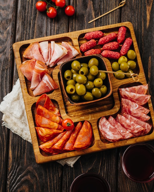 Foto lanches para vinho em uma placa de madeira menazhnitsa com azeitonas de salsicha e tomate cereja