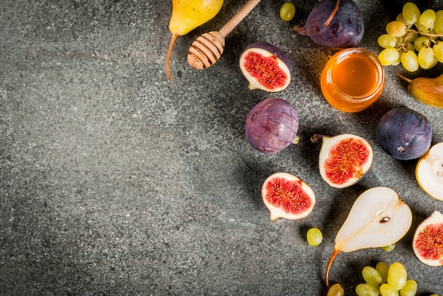 Lanches, sobremesas veganas dietéticas. Outono frutas figos, peras, uvas com mel em uma mesa de pedra preta. vista superior copyspace