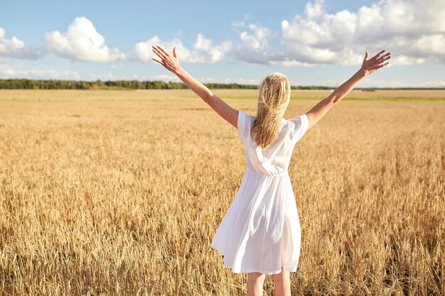 Land-, Natur-, Sommerferien-, Urlaubs- und Menschenkonzept - glückliche junge Frau im weißen Kleid auf dem Getreidefeld