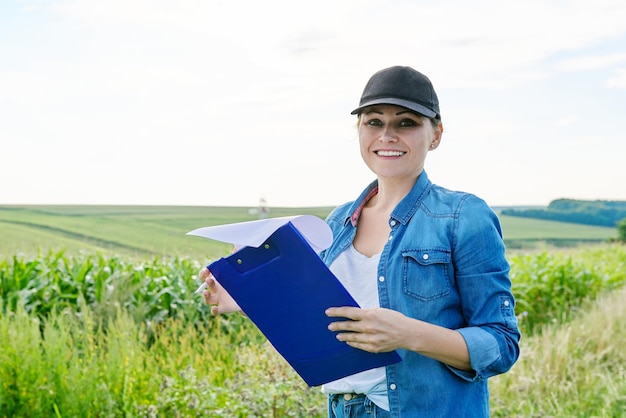 Landarbeiterin mit arbeitsordner im grünen maisfeld, frau, die auf dem bauernhof arbeitet, analysiert die ernte, kopierraum